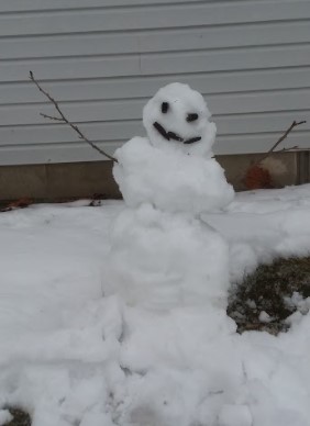 A small snowman made with two sticks and mulch.
